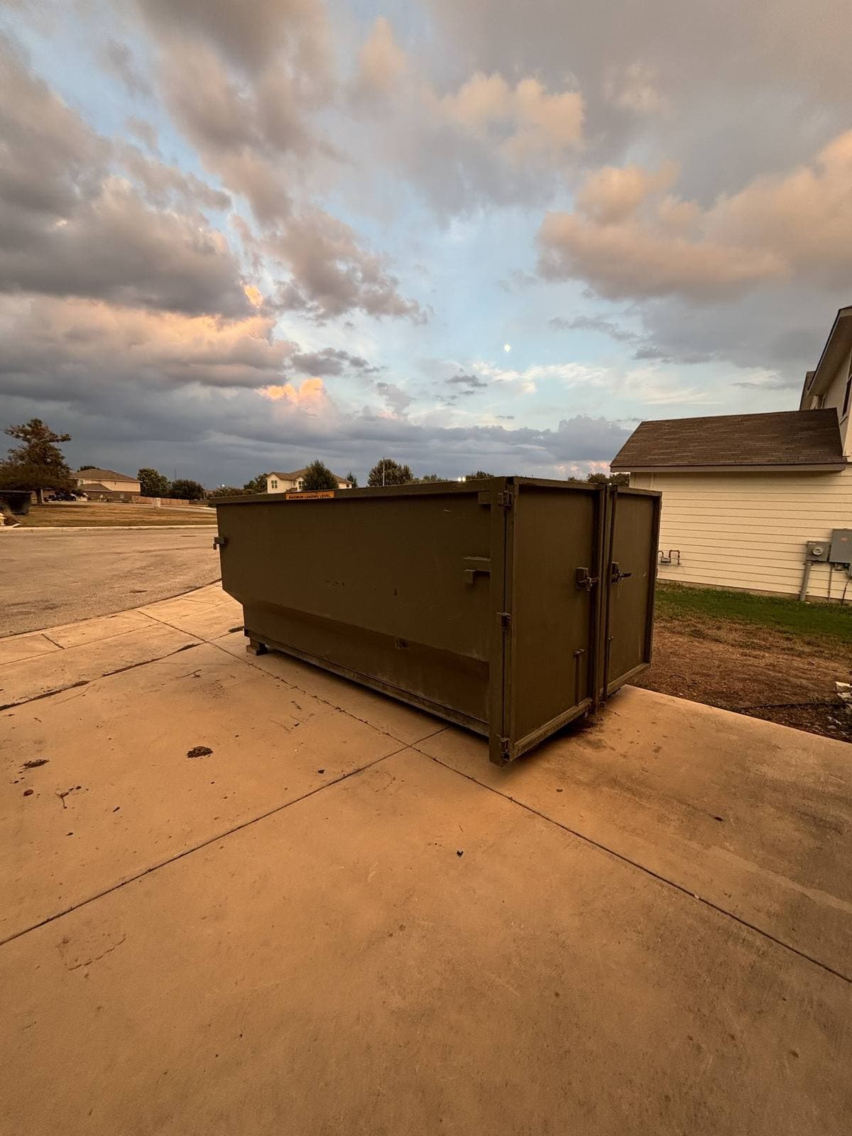 Taylor & Taylor roll-off dumpster on a residential driveway under an evening sky